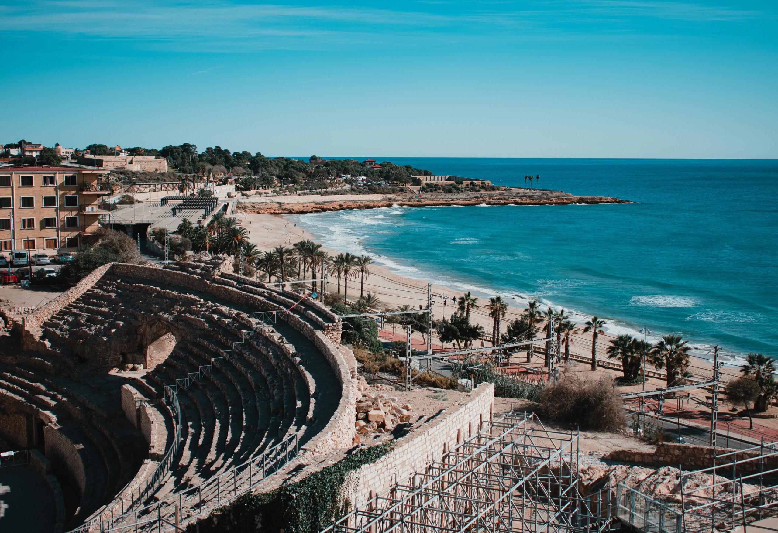 Stunning aerial view of Tarragona amphitheater with coastal shoreline, palm trees, and clear blue sea in Spain.